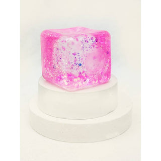 Pink and white speckled cube on a white stand with a white background