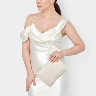 Woman wearing a white satin dress holding a matching clutch against a white background