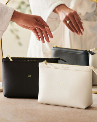 Two black and white bags with gold zippers on a neutral background