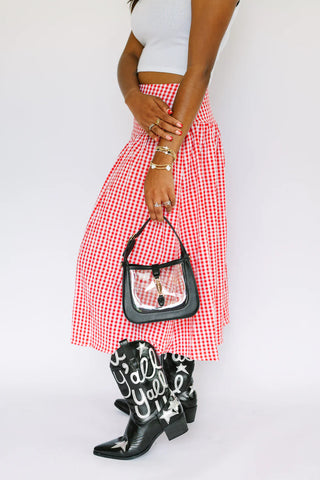 Person wearing a red and white checkered skirt, white top, black boots with white text, and holding a black handbag.